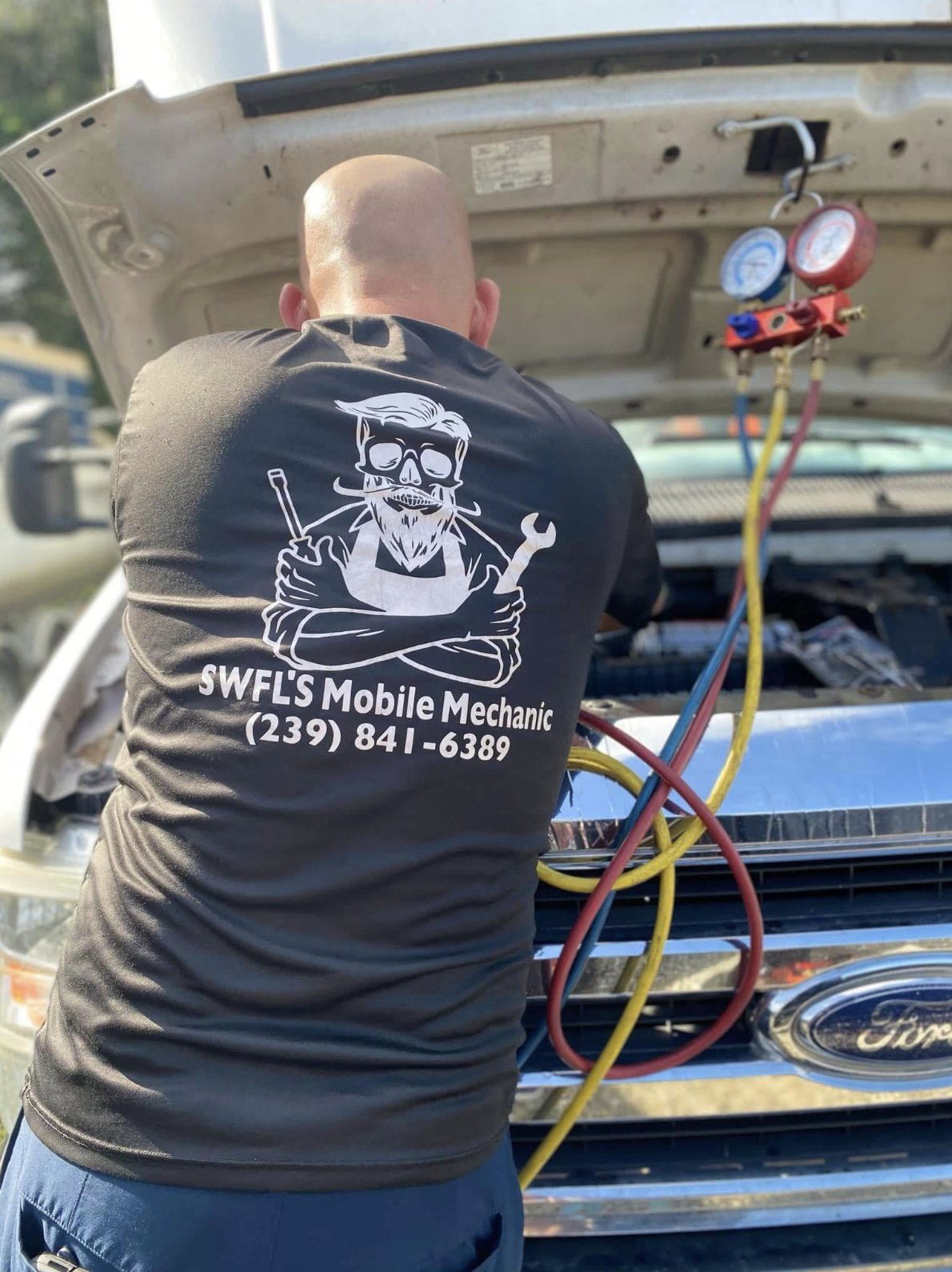 Mechanic in Swfl's Mobile Mechanic shirt servicing an A/C system on-site